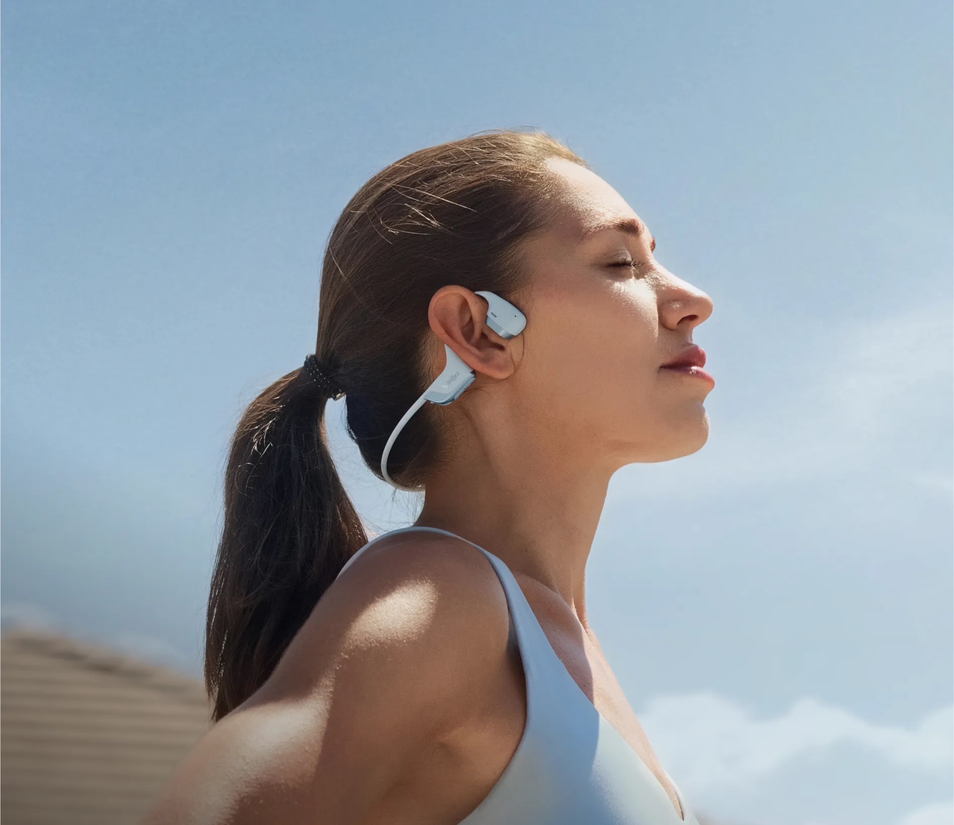 Runner wearing Shokz open-ear headphones under a clear blue sky